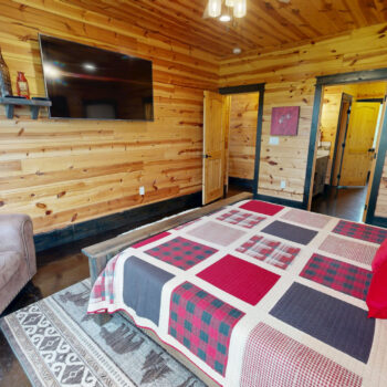 Cozy wooden cabin bedroom with a quilted bed and TV.