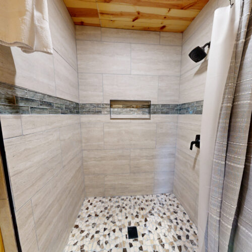 Modern walk-in shower with pebble floor and white tiled walls.