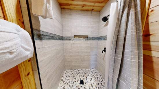 Modern walk-in shower with pebble floor and white tiled walls.