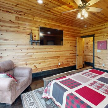 Cozy wooden bedroom with a patterned quilt and mounted TV.