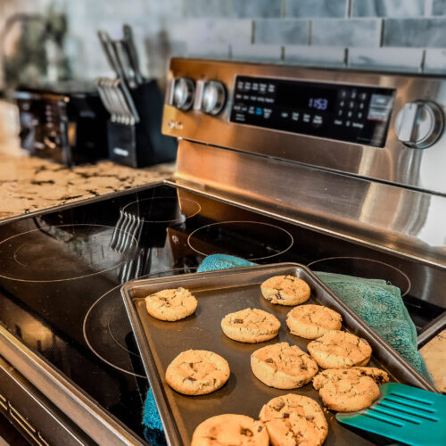 Freshly baked chocolate chip cookies cooling on a stove.