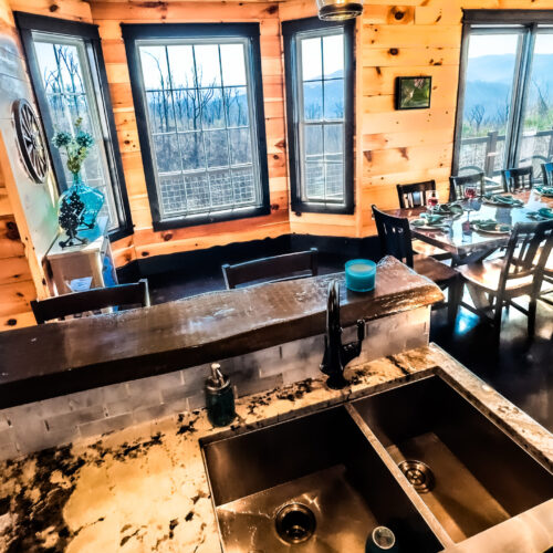 Cozy rustic kitchen with wooden beams and large windows overlooking greenery.