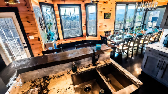 Cozy rustic kitchen with wooden beams and large windows overlooking greenery.