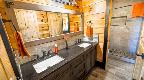Rustic bathroom with wooden walls and double sink vanity.