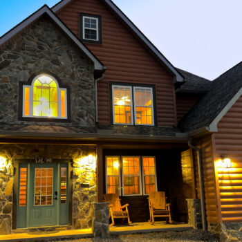Cozy house entrance warmly lit at dusk with rocking chairs on the porch.