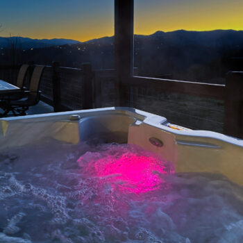 Hot tub glowing pink during sunset with mountain views.
