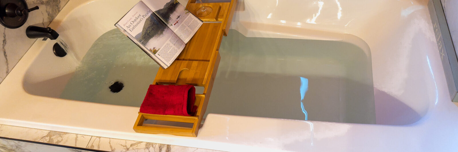 A bathtub with a wooden tray holding a book and towels.