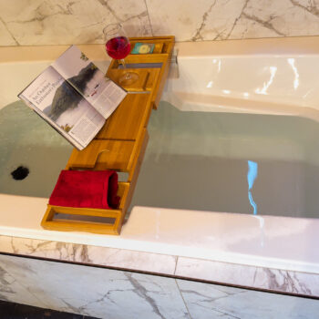 A bathtub with a wooden tray holding a book and towels.
