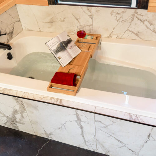 Luxurious bathtub setup with a wooden tray holding a book, a glass of wine, and a candle.