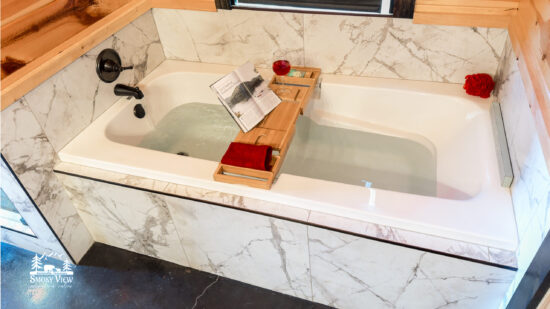 Luxurious bathtub setup with a wooden tray holding a book, a glass of wine, and a candle.