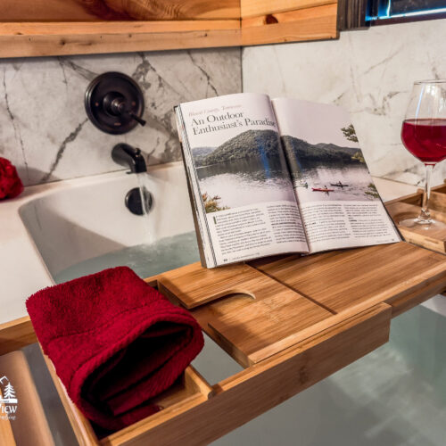 A cozy setup with a book, wine glass, and folded towel on a wooden bath tray.