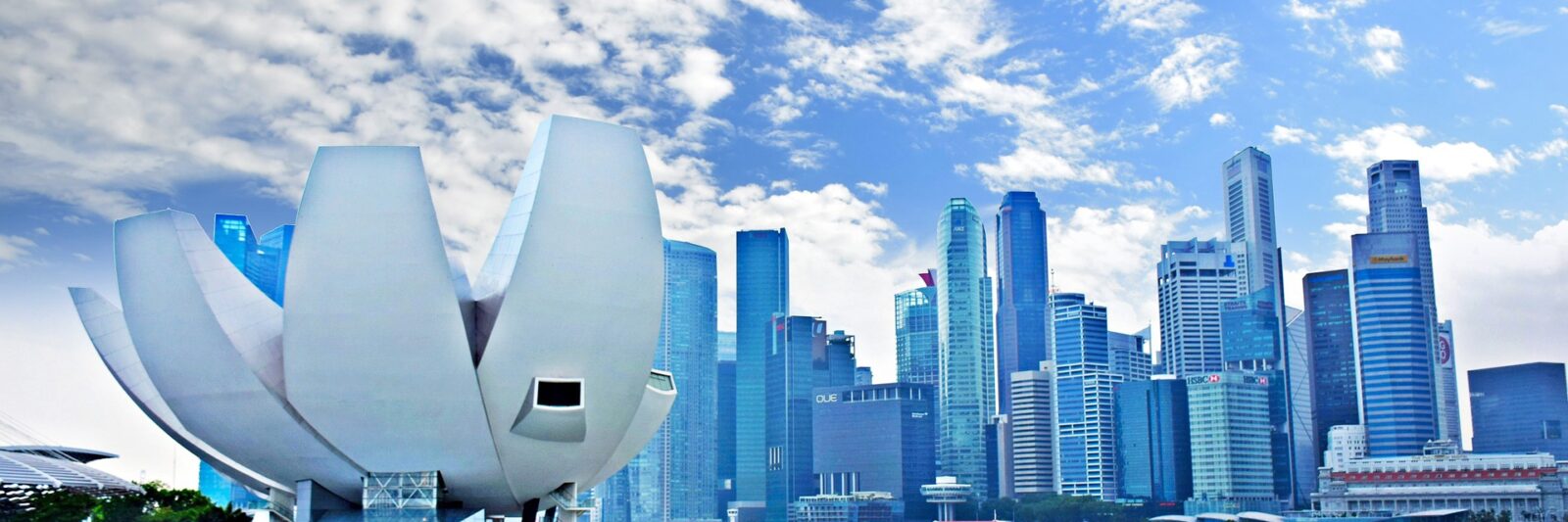 City skyline with unique white lotus-shaped building by the water under a partly cloudy sky.