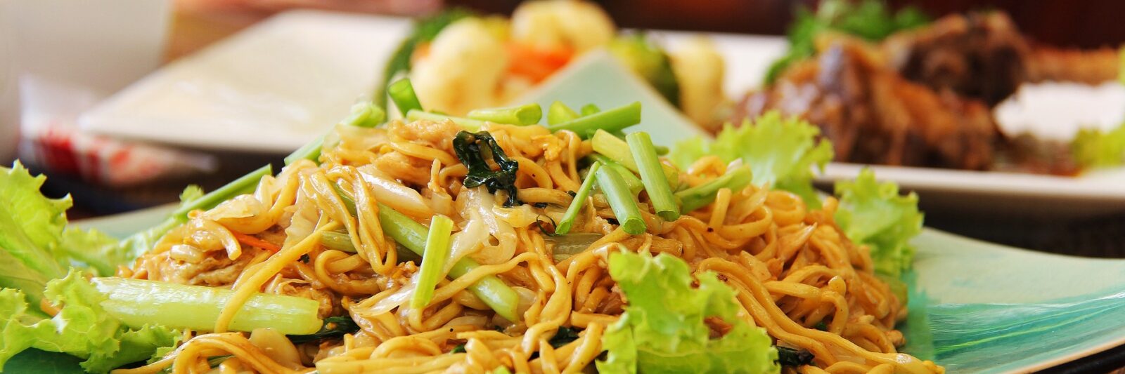 Plate of stir-fried noodles with vegetables and lettuce.